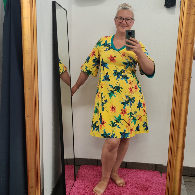 Gul plus size kjole i a-form med v-hals. Kjolen har blomster og guldsmede.