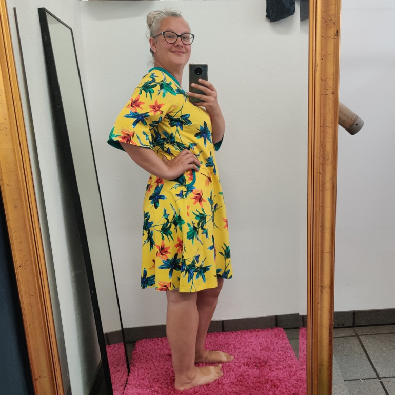 Gul plus size kjole i a-form med v-hals. Kjolen har blomster og guldsmede.