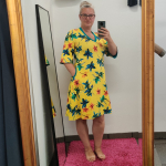 Gul plus size kjole i a-form med v-hals. Kjolen har blomster og guldsmede.